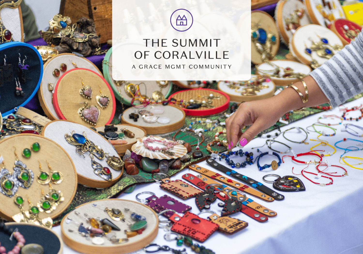 Hand reaches for blue beaded bracelets among a colorful jewelry display at a market stall.