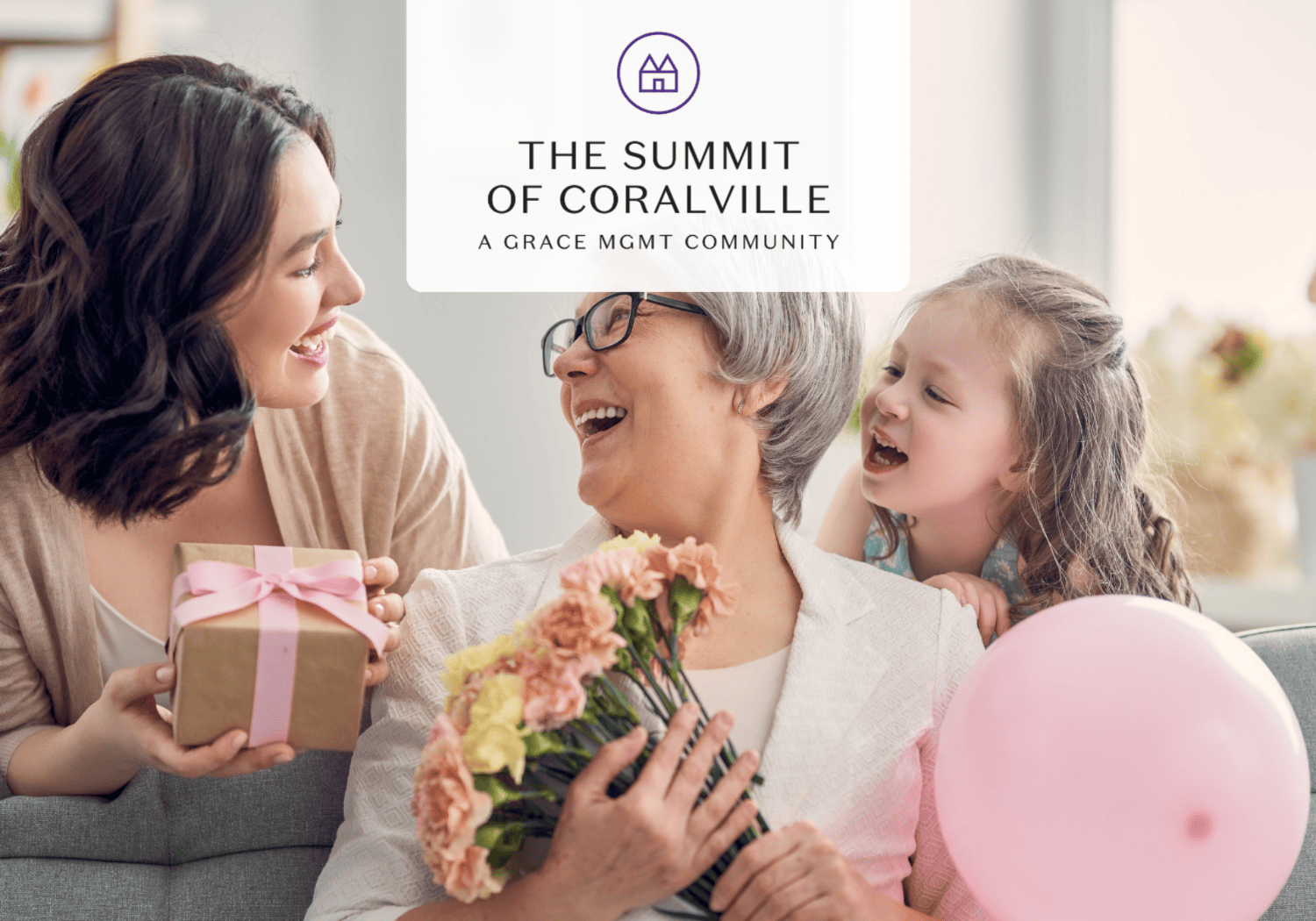 Three generations celebrate indoors: an older woman with flowers, a younger woman presenting a wrapped gift, and a smiling child with a pink balloon, under a 'The Summit of Coralville' banner.