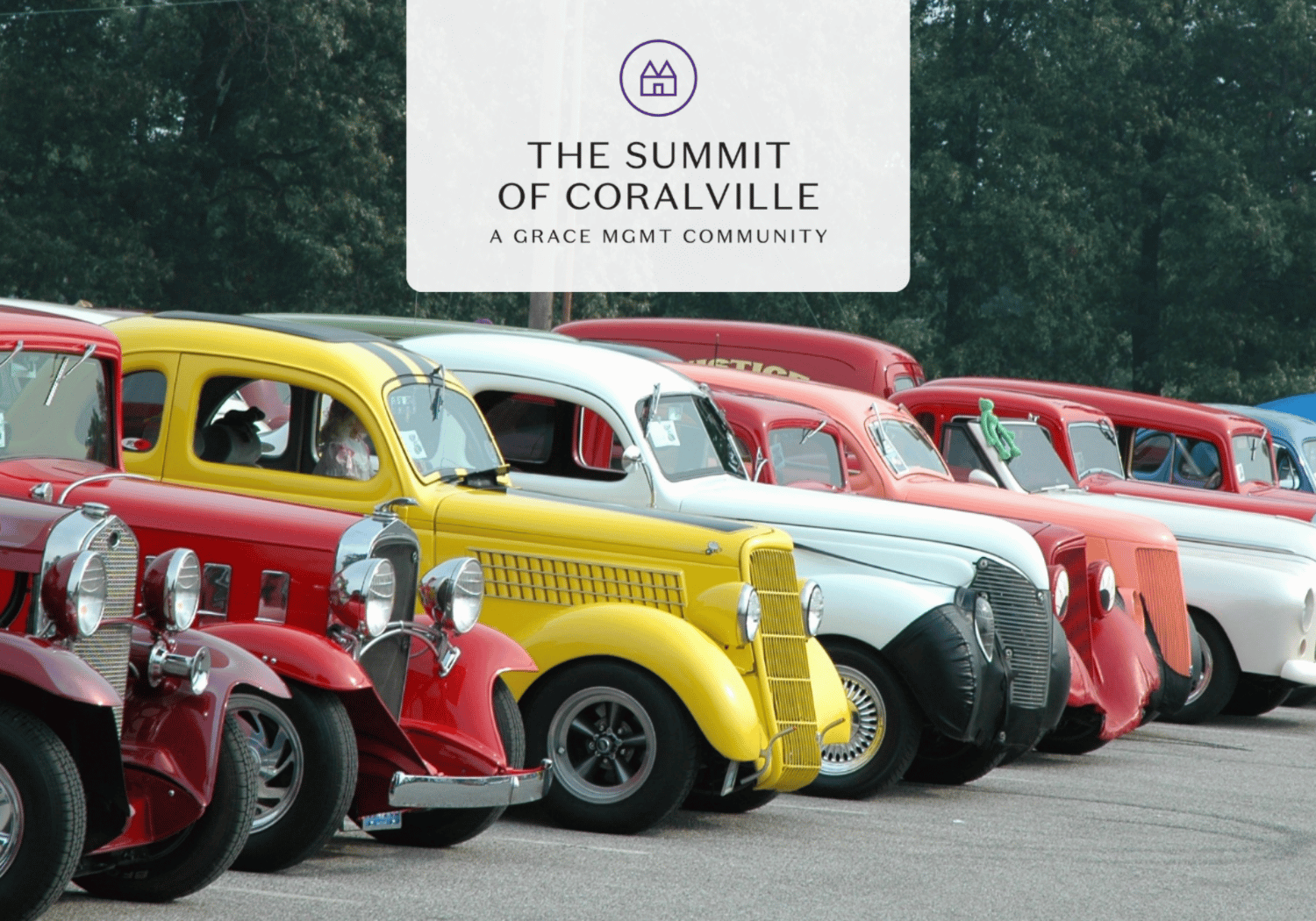 Row of colorful vintage cars parked at a car show beneath a white banner reading 'The Summit of Coralville'.